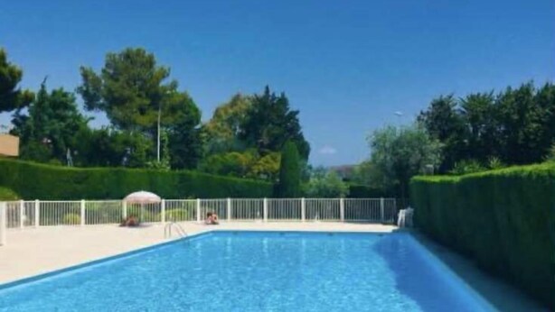 Una piscina con una cerca blanca, rodeada de setos y árboles bien recortados.