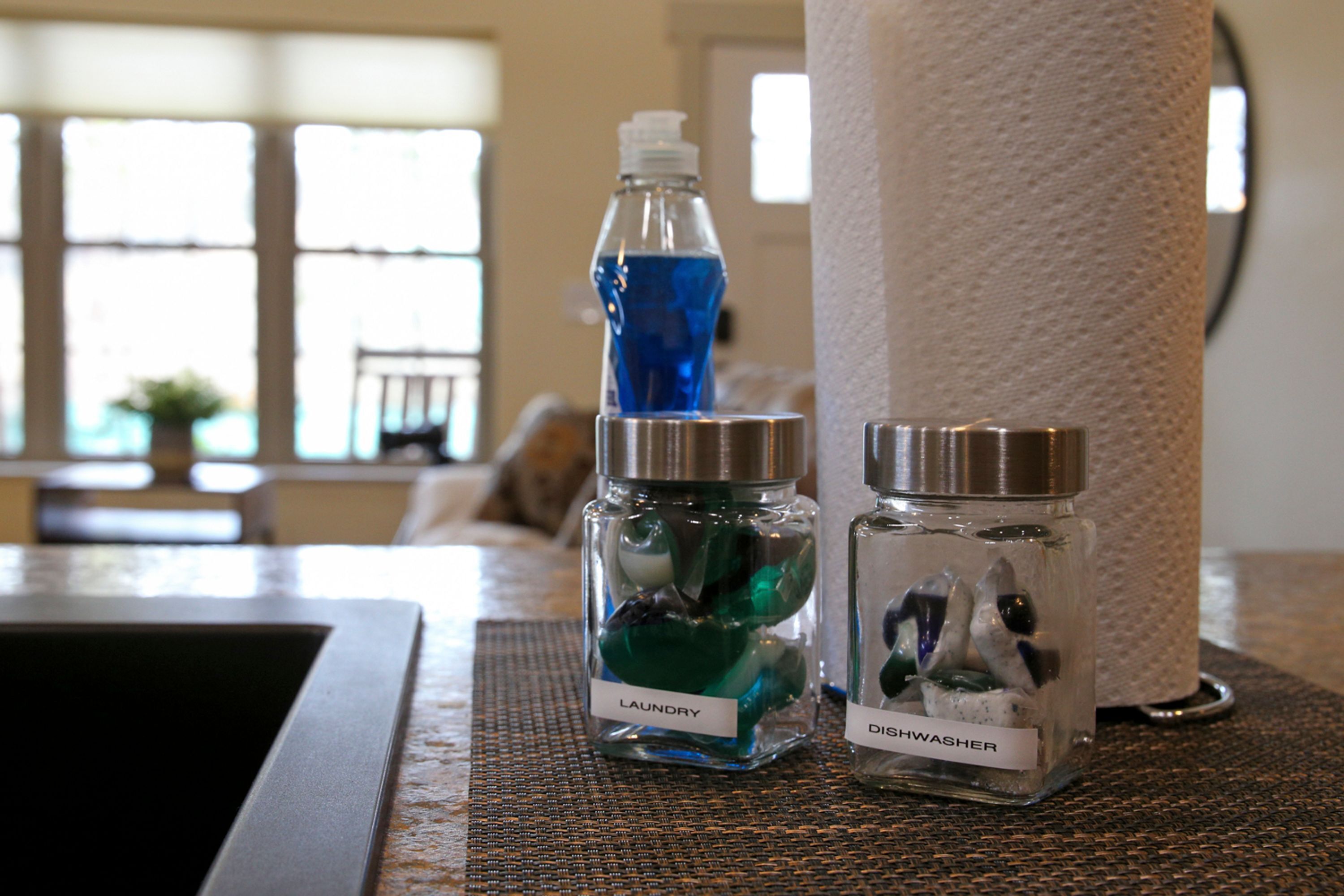 A bathroom counter with a bottle of laundry detergent, a bottle of dishwashing liquid, and a paper towel holder.