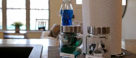 A bathroom counter with a bottle of laundry detergent, a bottle of dishwashing liquid, and a paper towel holder.