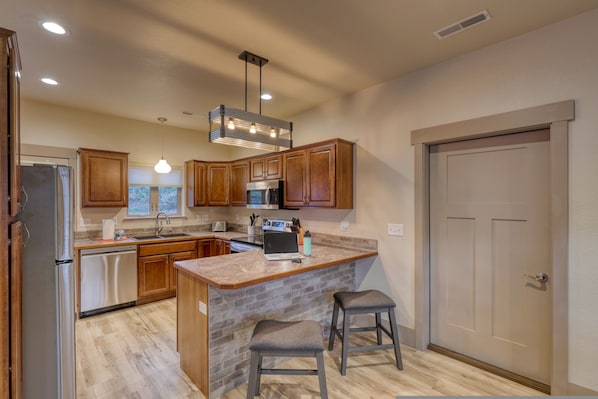 A modern kitchen with wooden cabinets, stainless steel appliances, and a granite countertop island with stools. - Washington s Quarters A Presidential Retreat (Rapid City)