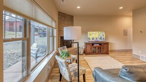 A spacious living room with a large window, a fireplace, a flat-screen TV, and a leather sofa.