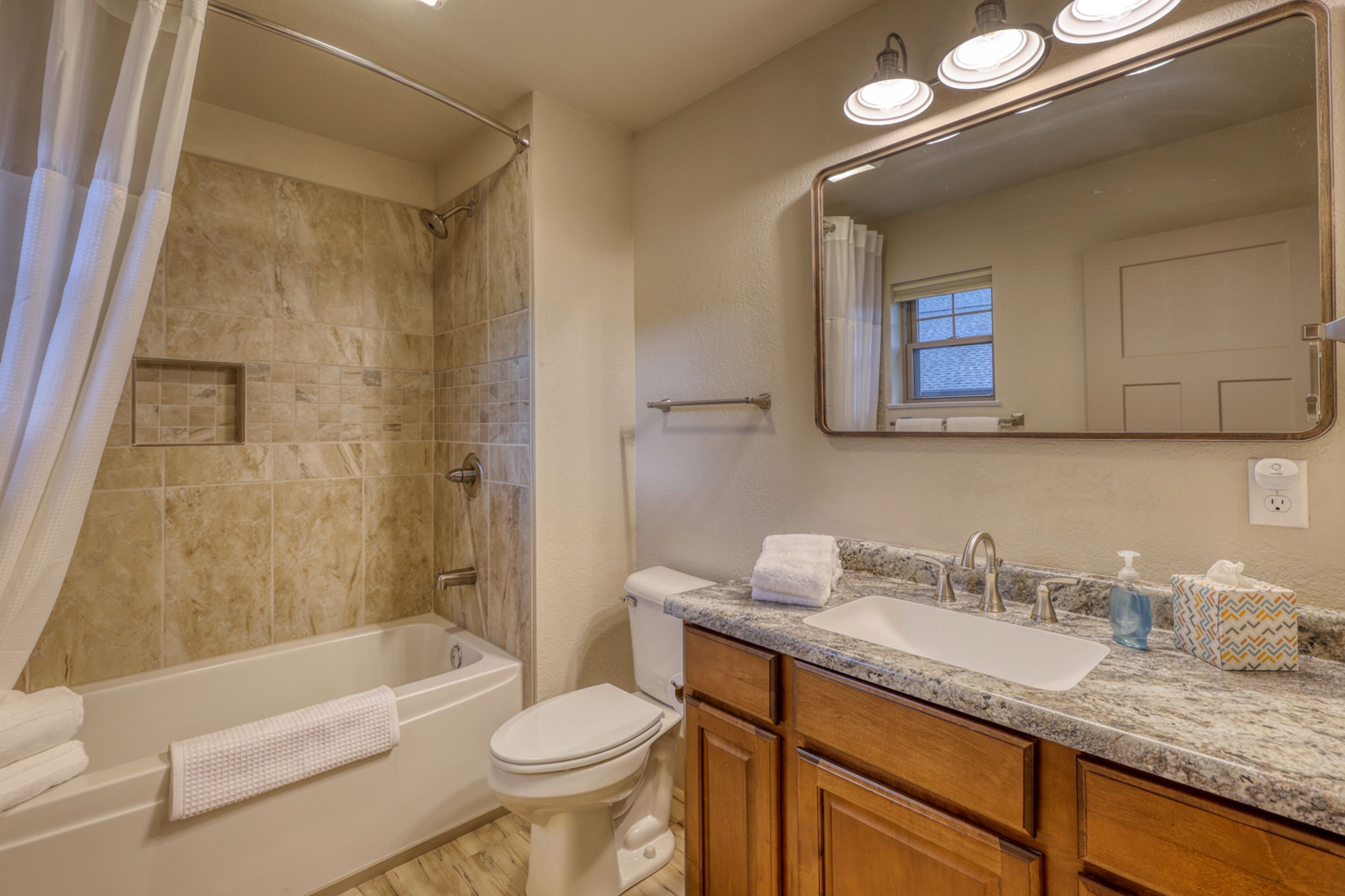 A bathroom with a bathtub, toilet, vanity with a sink, and a large mirror.