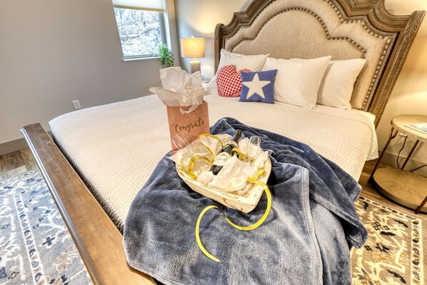 Un lit parfaitement fait, agrémenté d’un panier-cadeau avec le message « Félicitations », d’une serviette bleue et d’une bouteille de champagne.