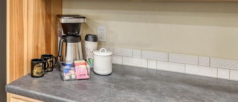 A kitchen counter with a coffee maker, mugs, and a coffee storage container.