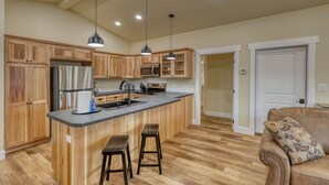 A spacious kitchen with wooden cabinets, a central island with stools, stainless steel appliances, and pendant lighting. - Throttle Down in Style A Biker s Dream Stay (Rapid City)