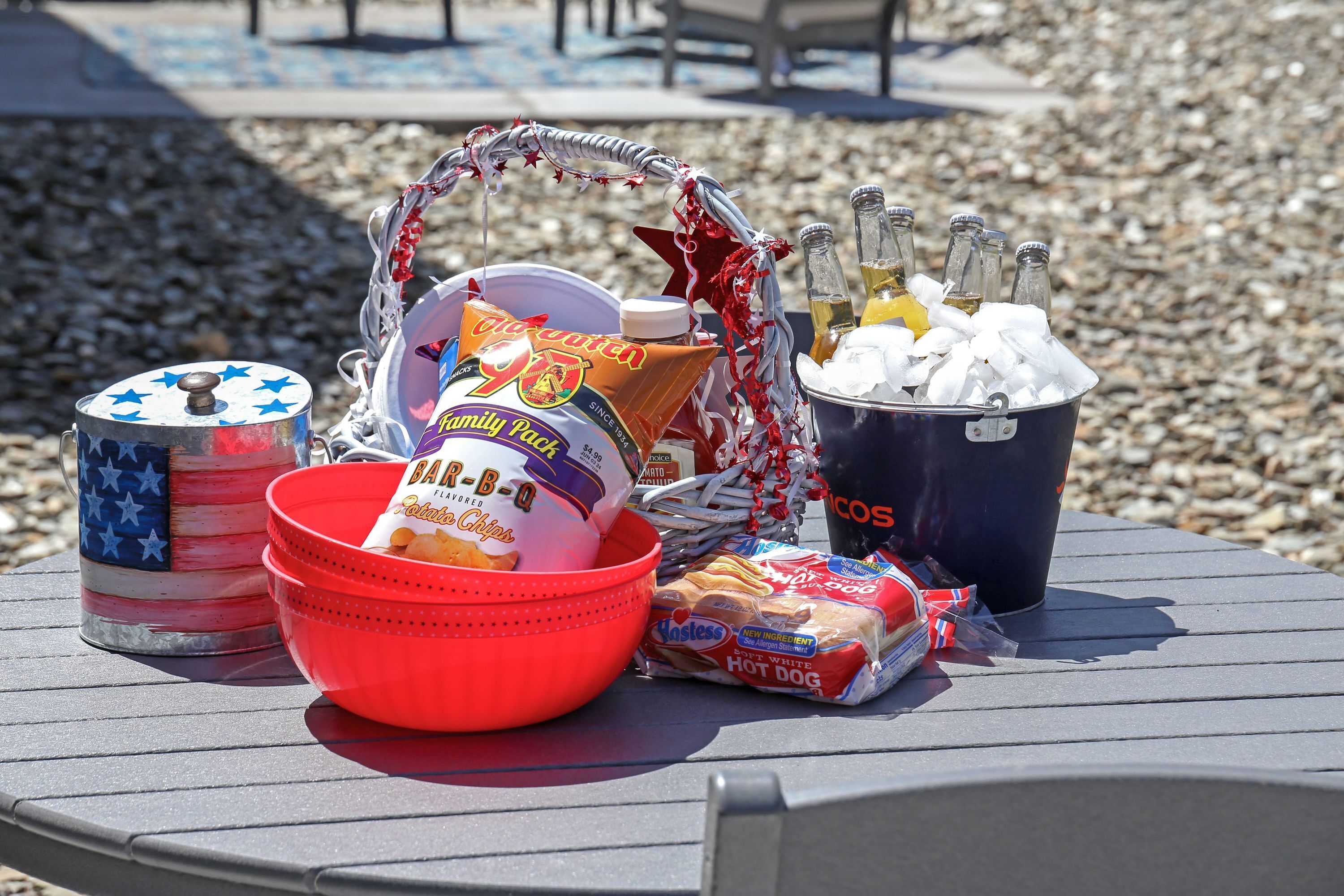 A table with a variety of food items and drinks, including a bucket of ice, a cooler, and a basket with snacks.