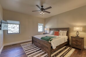 Un dormitorio con una cama de madera, un ventilador de techo, dos mesitas de noche con lámparas y un ventanal con persianas.