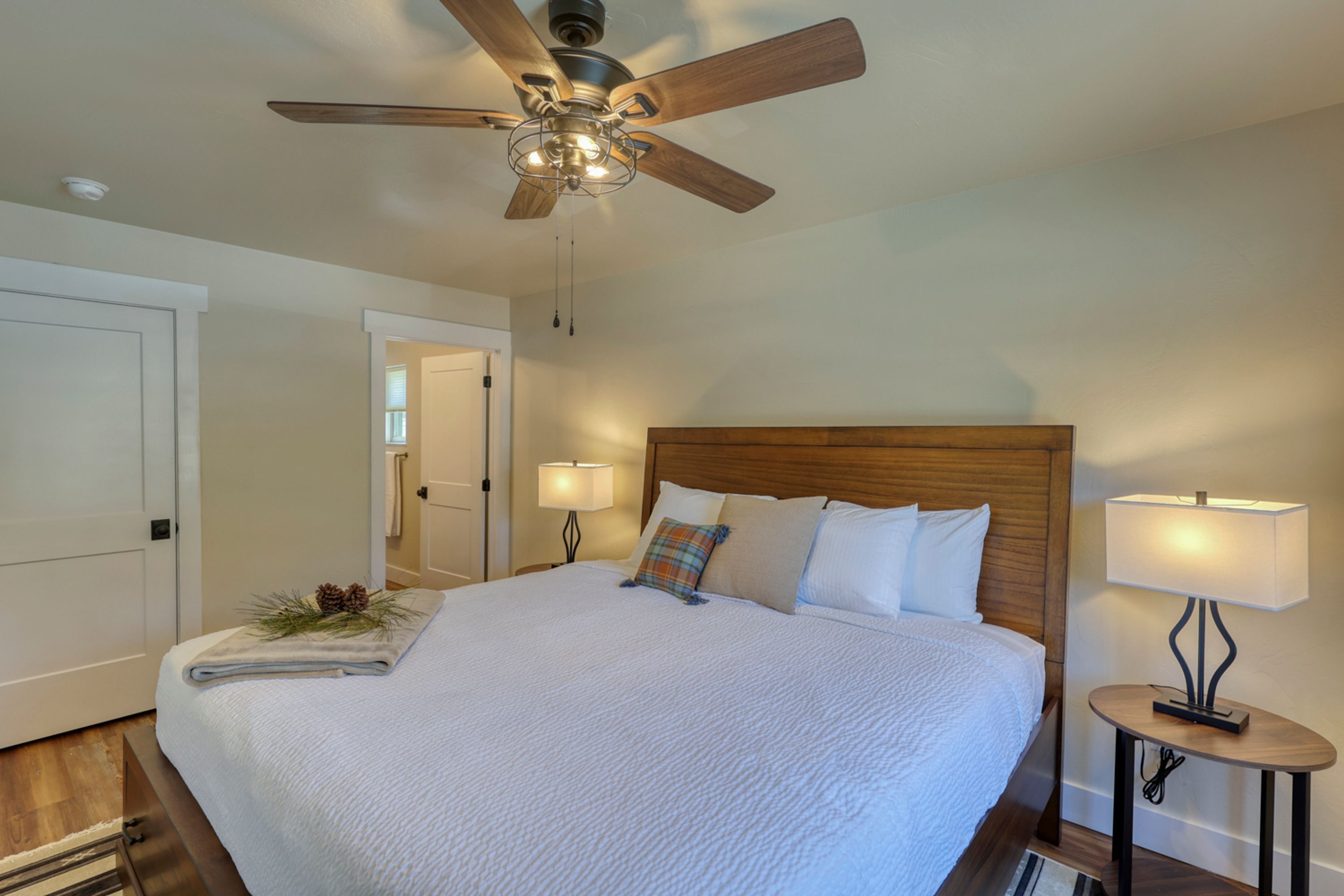 A neatly made bed with a wooden headboard, two bedside lamps, and a ceiling fan.