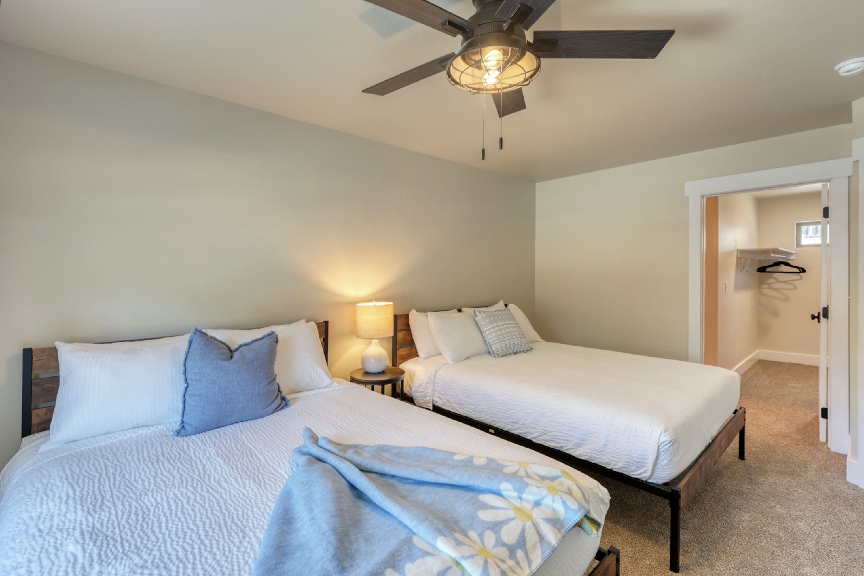 A bedroom with two beds, a ceiling fan, and a nightstand with a lamp.