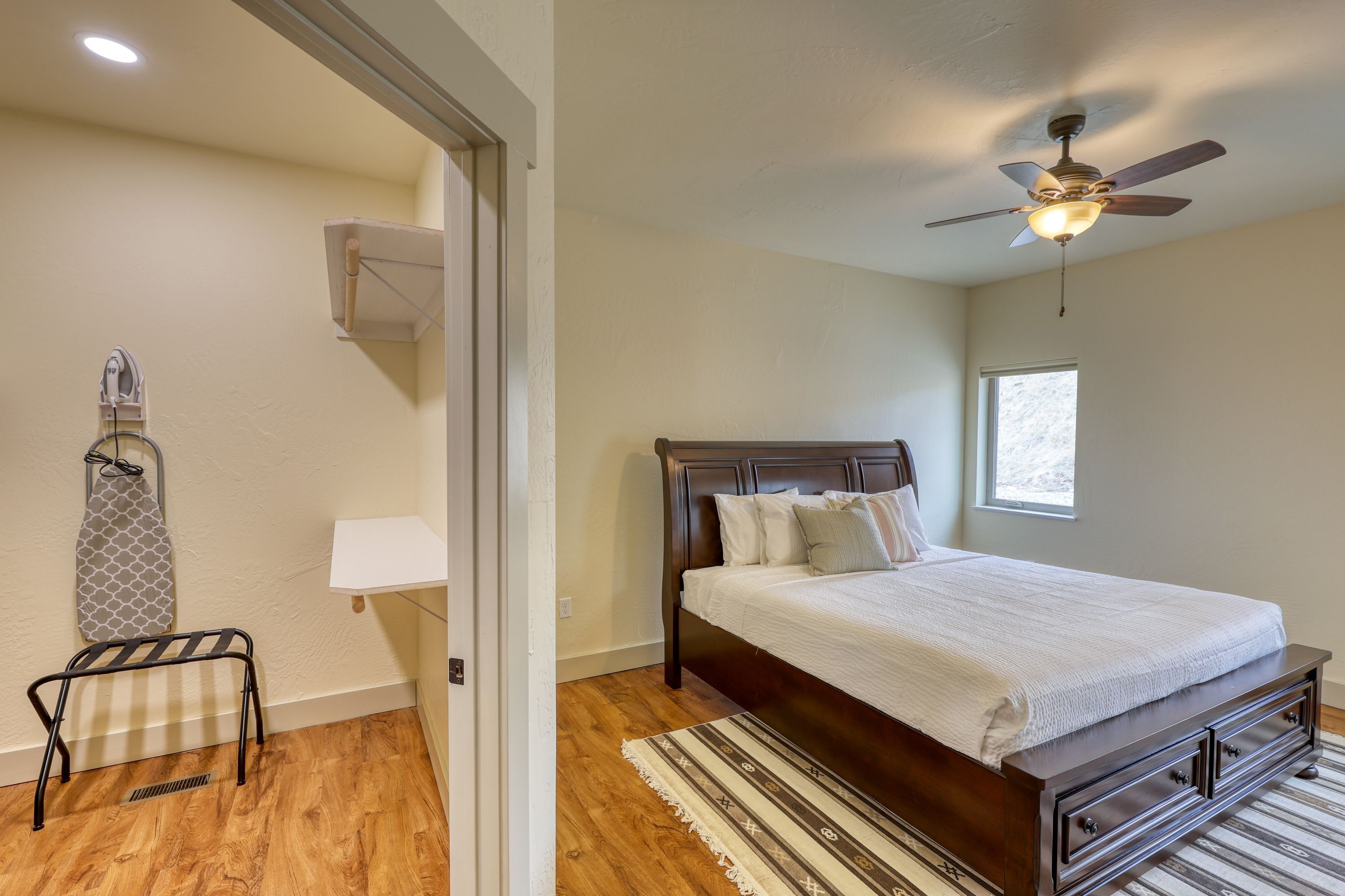 A bedroom with a wooden floor, a bed with a headboard, a ceiling fan, a window, and a radiator.