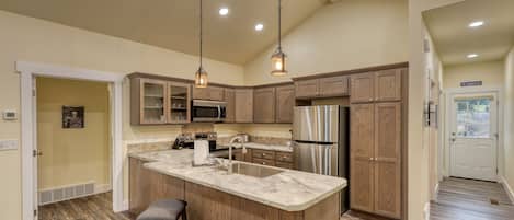A modern kitchen with wooden cabinets, stainless steel appliances, and a marble countertop.