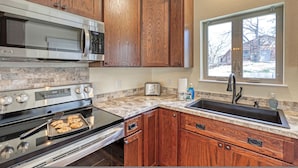 A kitchen with wooden cabinets, a stainless steel microwave, an oven, a sink, and a window with a view of a snowy landscape.