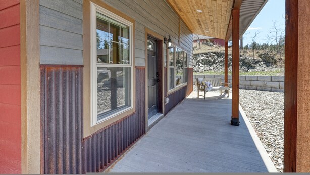 A covered porch with a wooden ceiling, large windows, and a bench.