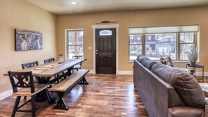 A dining area with a long wooden table and benches, a brown leather sofa, and a door with a bull head decoration. - Modern Condo Near BH Attractions-garage Parking (Rapid City)