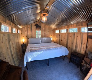 Un dormitorio estilo cabaña, acogedor, con una cama grande, paredes de madera y techo inclinado.