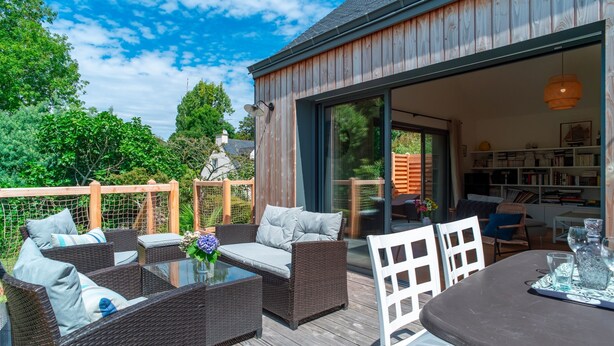 An outdoor deck with wicker furniture, a glass table, and a view of the house interior. - L'escale d'Erquy - Proche Plage (Erquy)