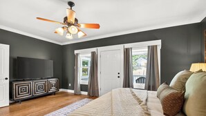 A bedroom with a bed, a ceiling fan, a TV, a dresser, and a view through a door. - 1921 Craftsman Bungalow · Charnwood Historic District (Tyler)