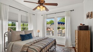 A bedroom with a bed, a ceiling fan, a dresser, and a view of the outdoors. - 1921 Craftsman Bungalow · Charnwood Historic District (Tyler)