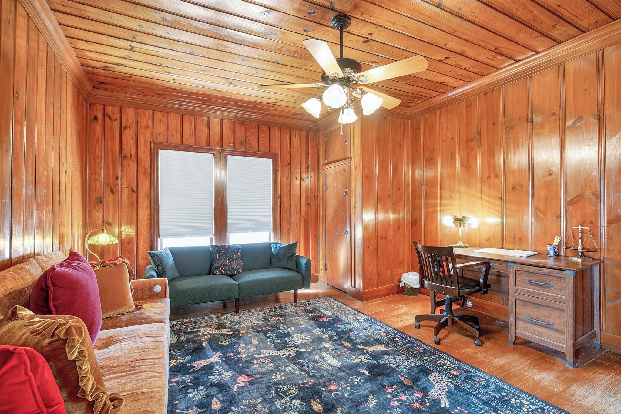 A room with wooden walls, a ceiling fan, a sofa, a desk, and a chair.