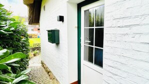 A white building with a green door, a window, and a thatched roof.