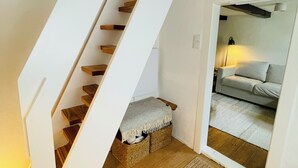 A staircase with wooden steps and a white wall. There is a small bench at the bottom of the stairs.