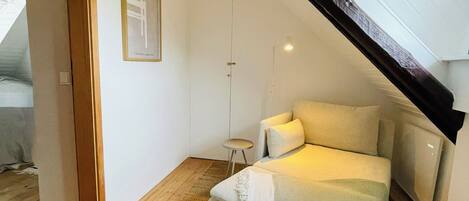 A cozy bedroom with a sloped ceiling, a bed, a small table, and a framed picture on the wall.