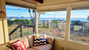 A cozy room with a sofa and a view of a fenced backyard. - Delightful 2-bedroom occuan view cottage , 5 minutes walk to the beach (Bodega Bay)