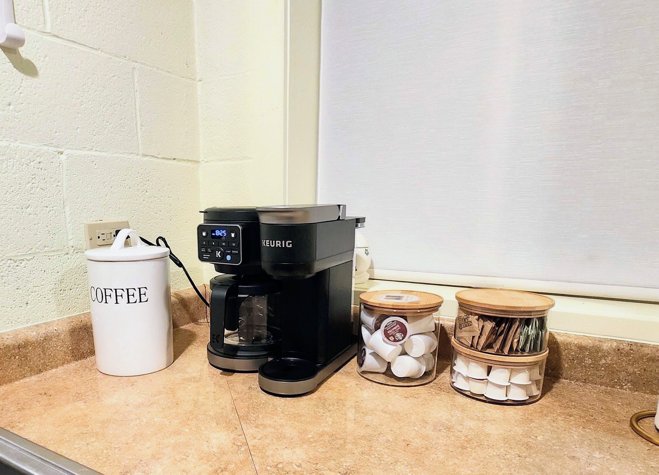 A coffee maker, a coffee container, and two jars of coffee pods on a kitchen counter.