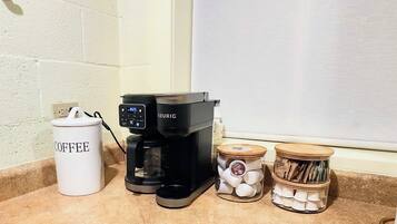 A coffee maker, a coffee container, and two jars of coffee pods on a kitchen counter.