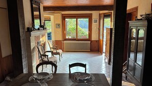 Un coin repas avec une table en bois dressée pour quatre personnes, une cheminée et une vue sur la verdure environnante.