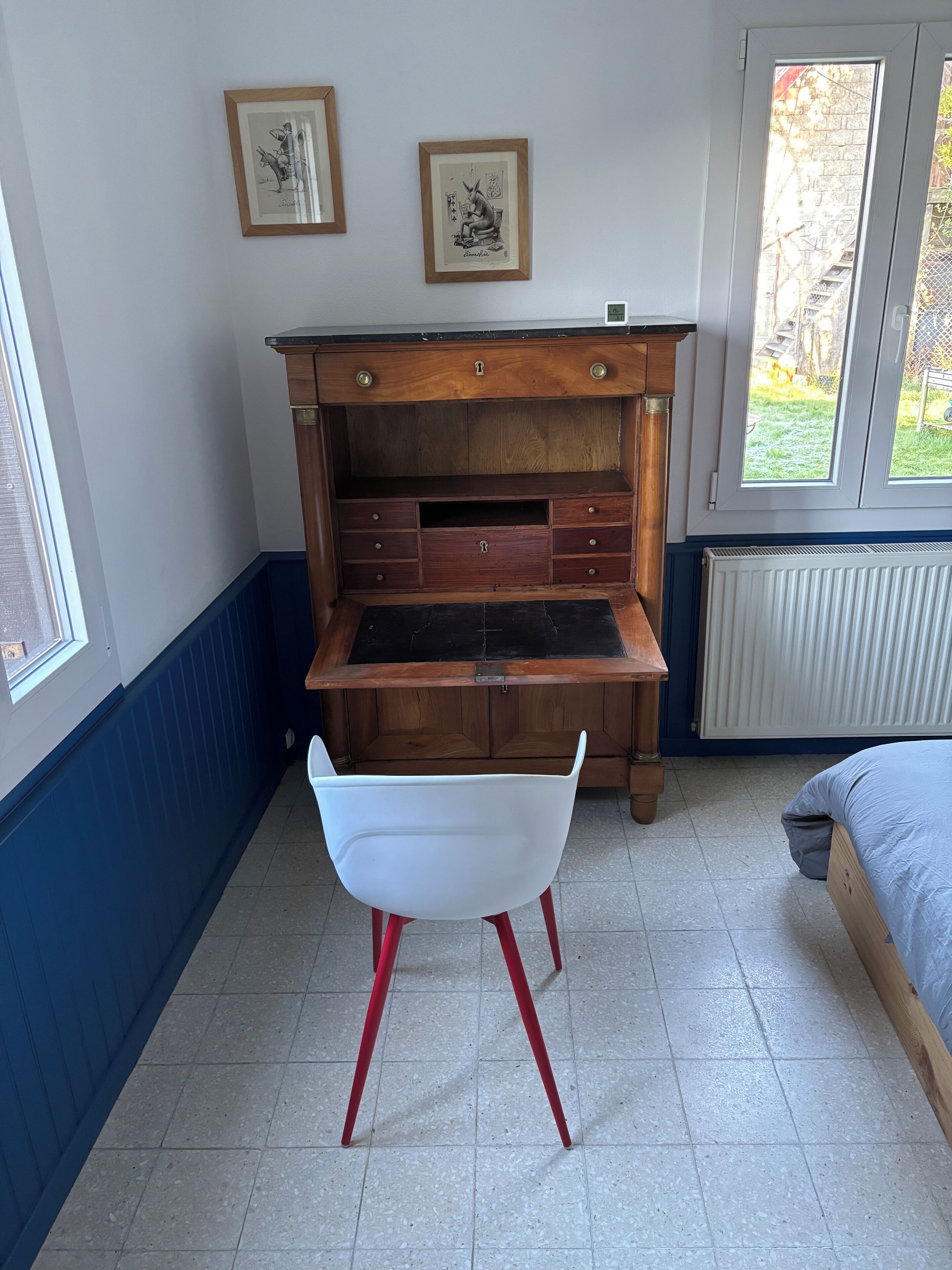 A room with a wooden desk, a white chair, a bed, and two framed pictures on the wall.