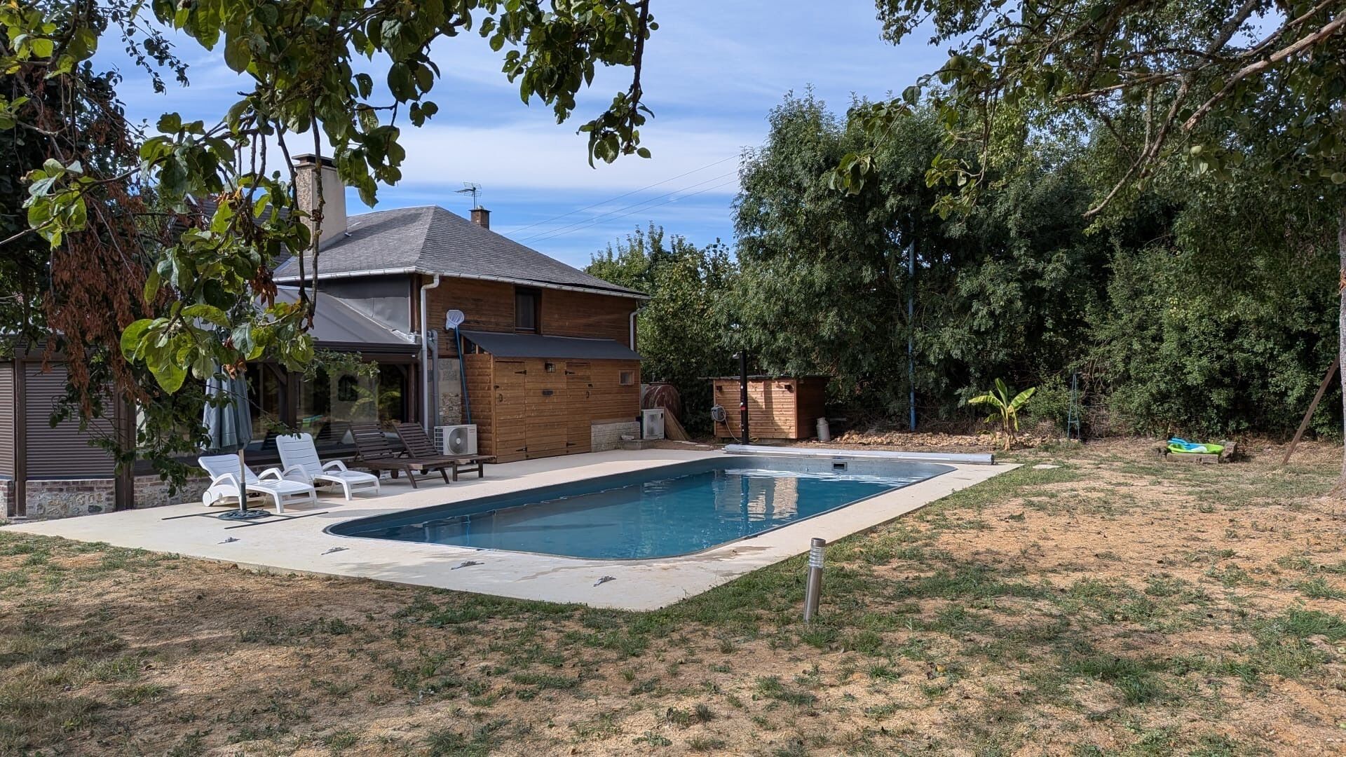 Un patio trasero con piscina, una casa de madera y un área de patio techada.