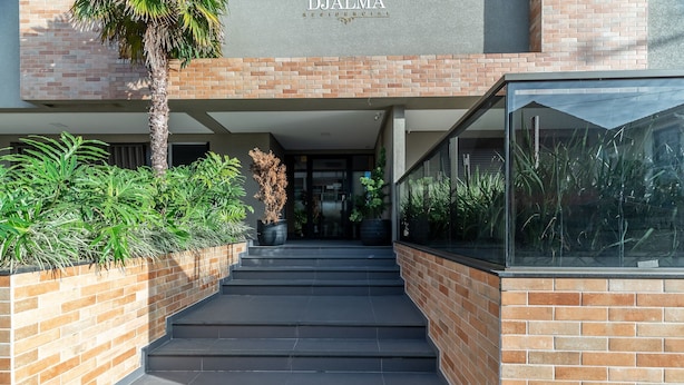 A modern building entrance with a brick facade, a palm tree, and a glass enclosure. - DRL - Apartments 300m From Bombinhas Beach (Bombinhas)