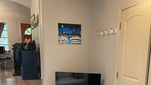 Een woonkamer met een televisie op een houten dressoir, een kamerbreed tapijt met dessin en een schilderij van een besneeerd landschap.