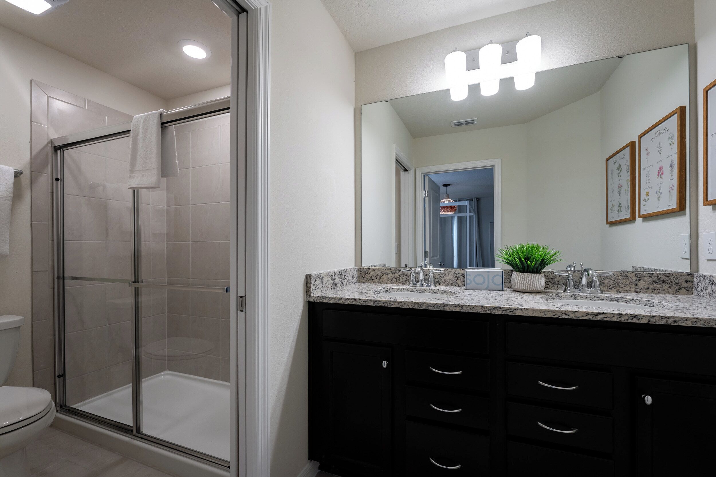 Une salle de bain moderne dotée d’une douche à parois de verre, d’un meuble-lavabo avec des placards noirs et d’un grand miroir surmonté d’un luminaire.