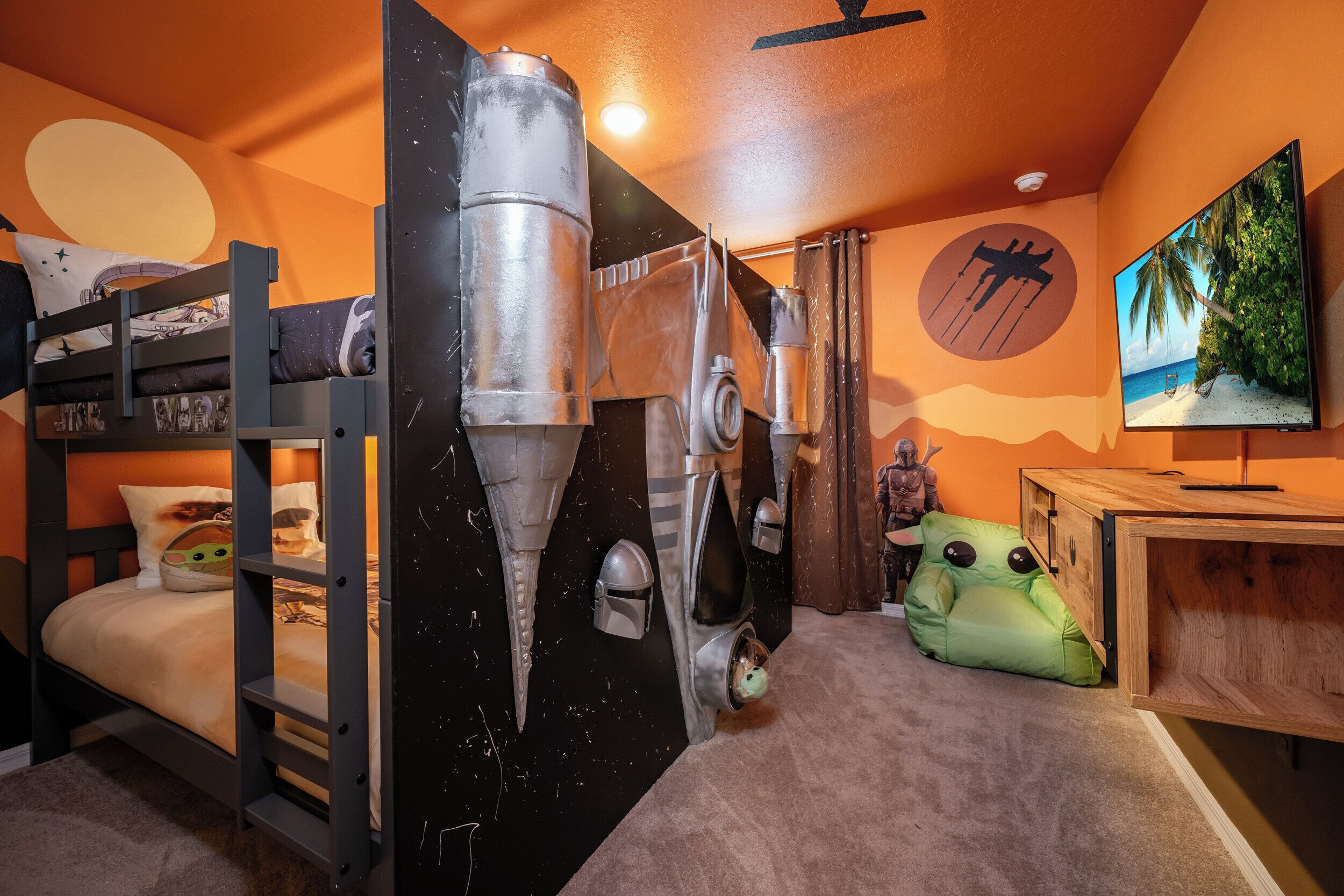 A bunk bed with a Star Wars-themed wall, a green plush toy, and a TV displaying a beach scene.