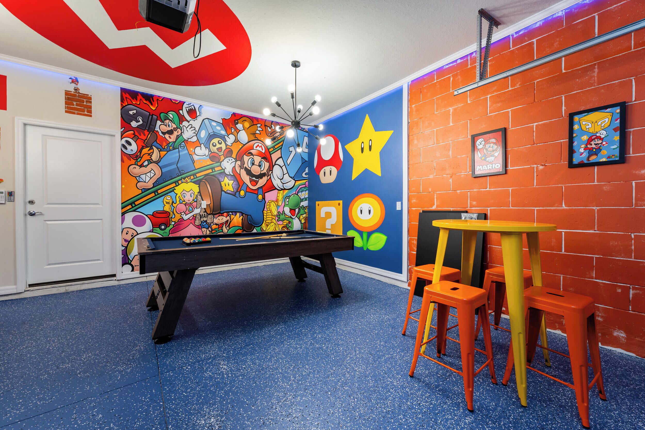 Une pièce avec une table de billard, des œuvres d’art colorées accrochées au mur et un mur en briques.