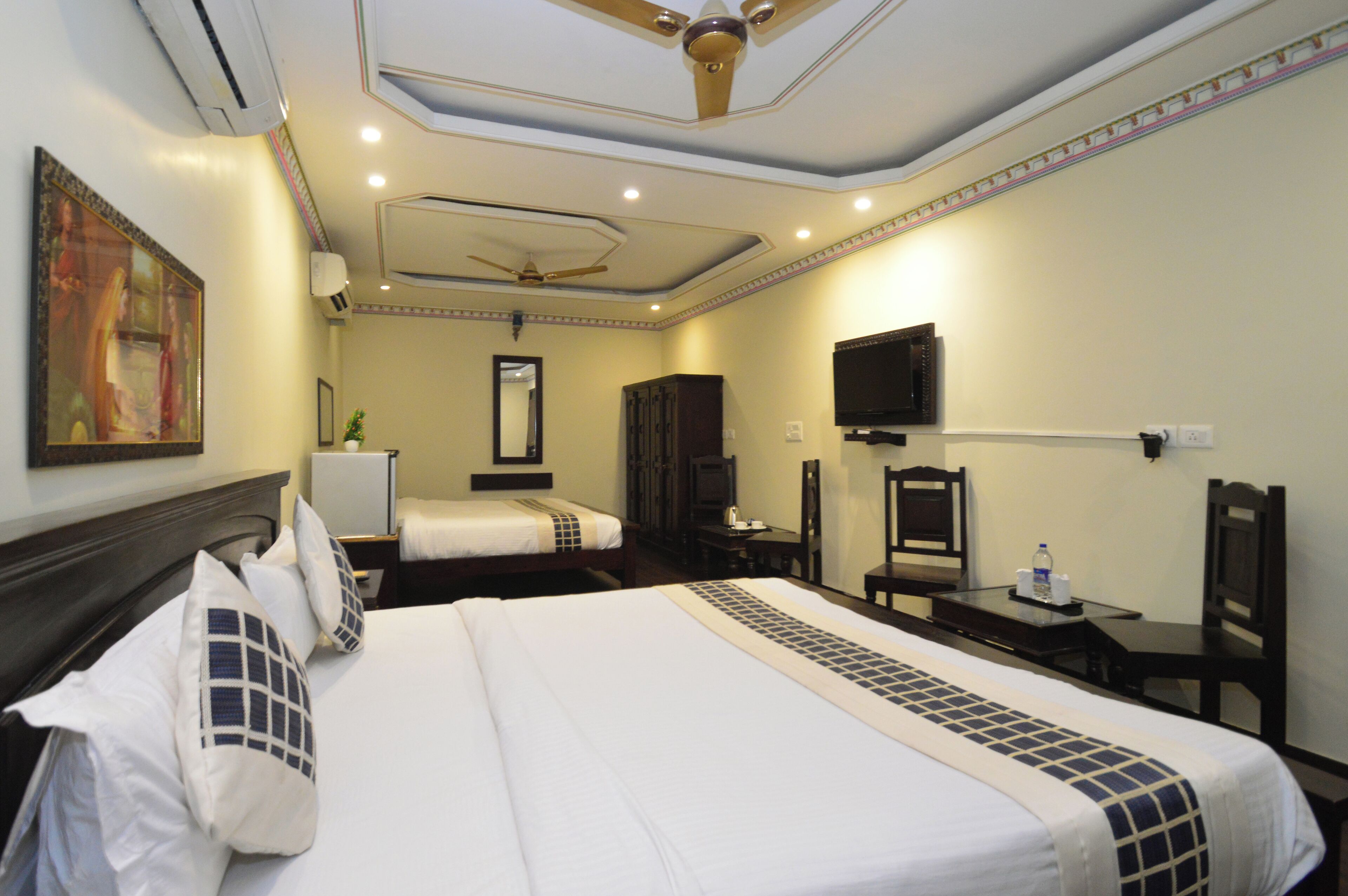 Una habitación de hotel con una cama grande, un escritorio, una silla, un televisor y un ventilador de techo.