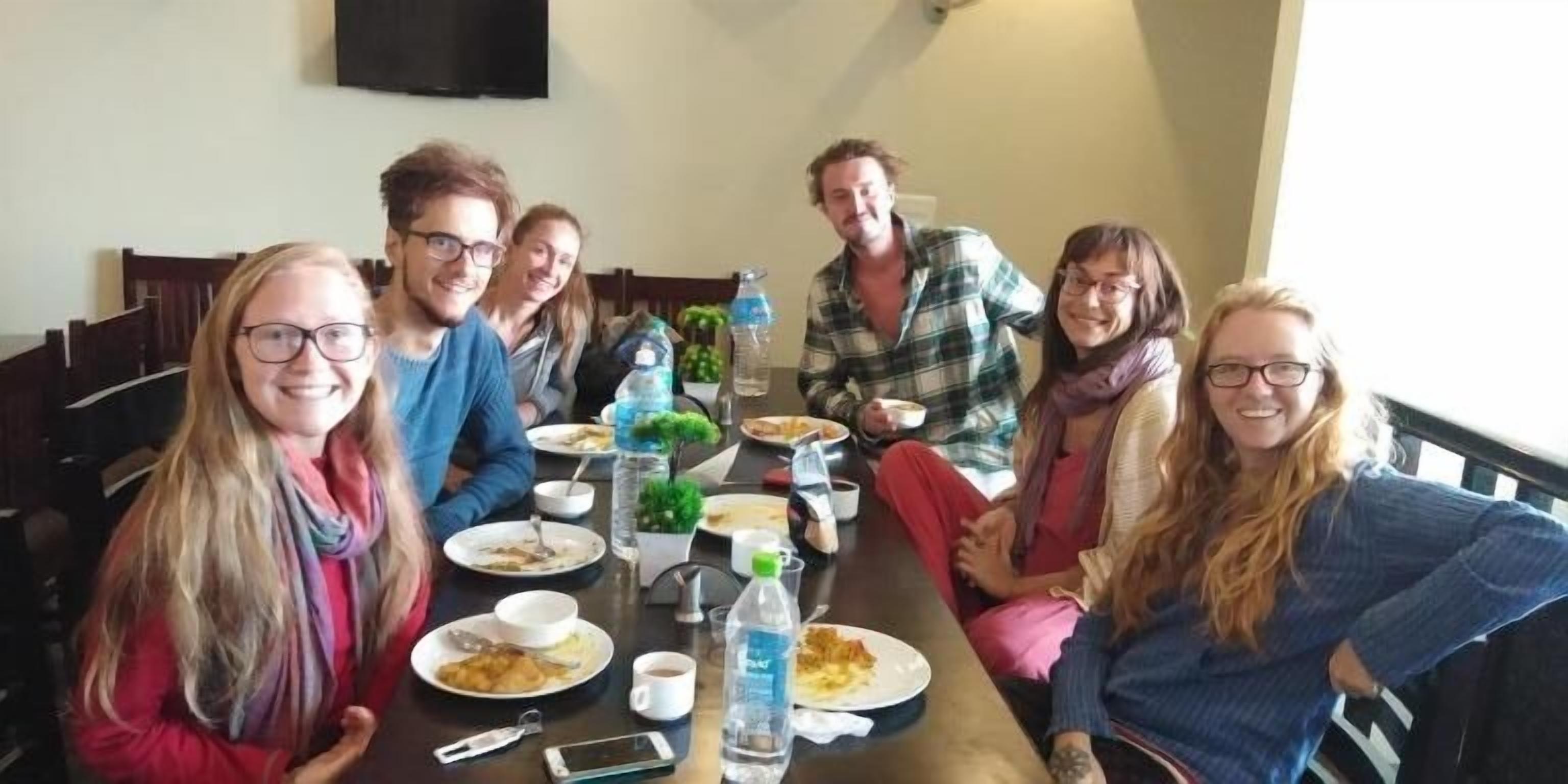 A group of people seated around a table with various dishes and drinks, indicating a meal setting.
