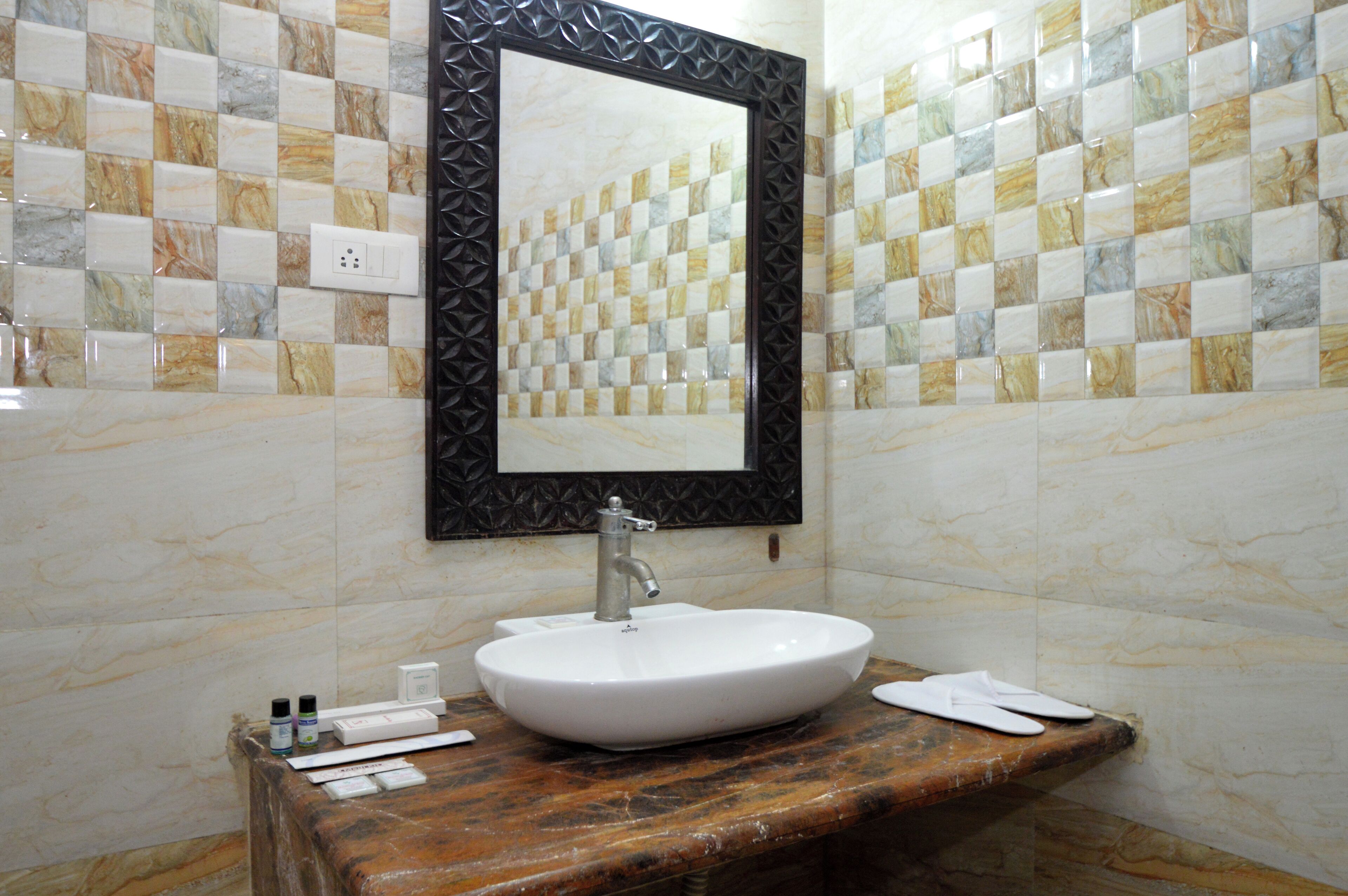A bathroom with a marble sink, a mirror with a decorative frame, and a tiled wall with a checkered pattern.