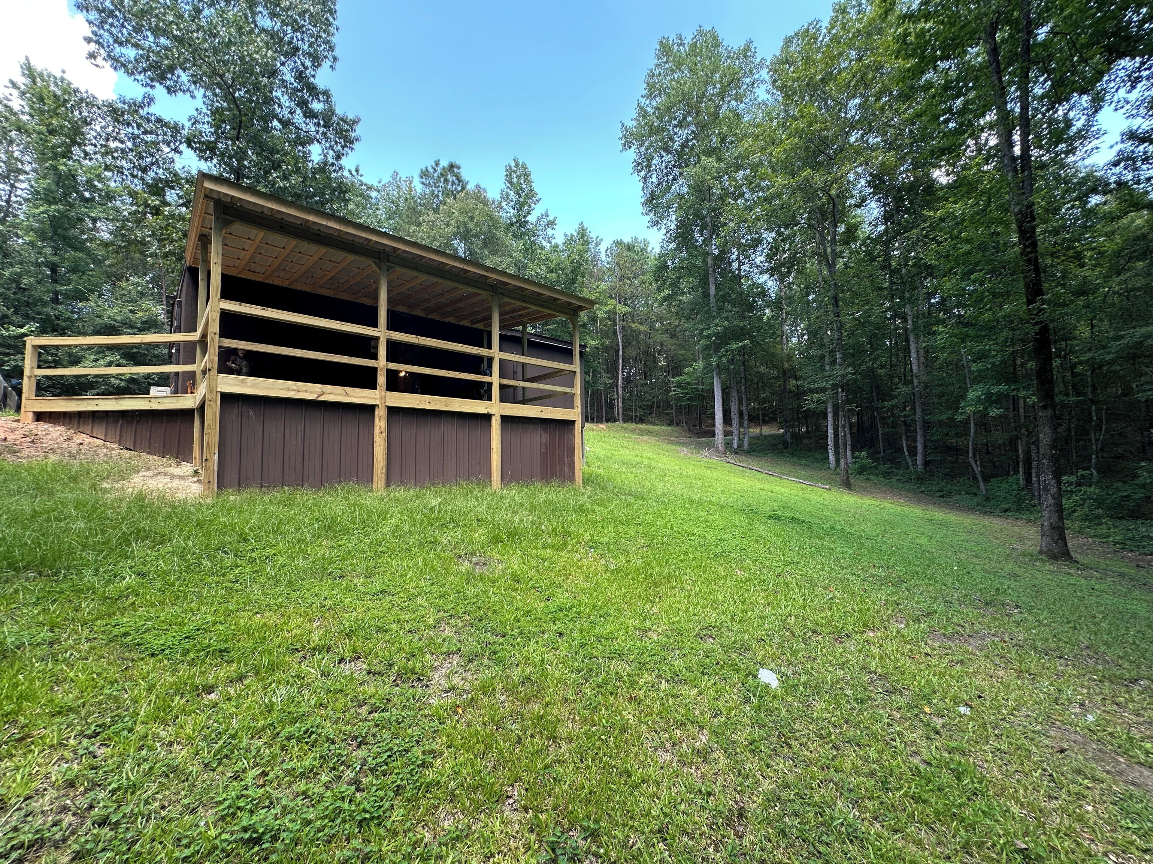 A wooden structure with a covered porch, surrounded by a grassy area and trees.