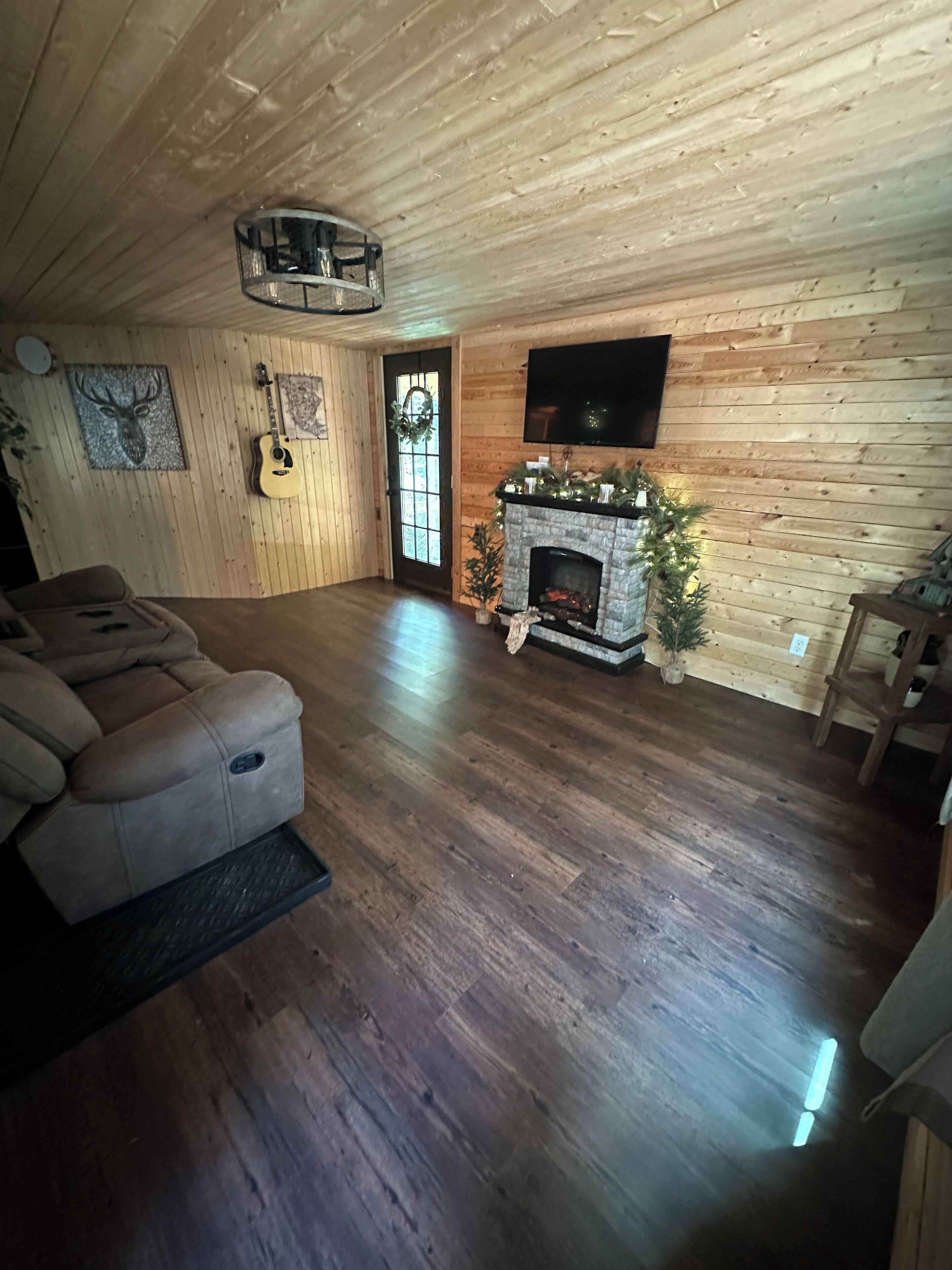 A cozy living room with a fireplace, wooden walls, a mounted TV, and a door with a wreath.