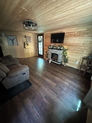 Een gezellige woonkamer met een open haard, houten wanden, een tv en een deur versierd met een krans.
