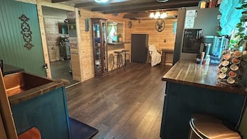 A rustic kitchen with wooden floors, hanging pots, and a bar area with stools.