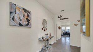 Un corridoio con un dipinto astratto moderno, un consolle con oggetti decorativi, uno specchio e un cartello con la scritta 'hello welcome'.