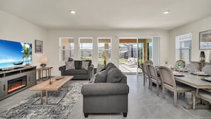 A spacious living room with a fireplace, a large flat-screen TV, a gray sofa, and a dining area with a table set for four. - Magical Family Getaway 7BD Villa with (Davenport)