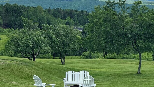 Un champ verdoyant avec des fauteuils Adirondack et un foyer.
