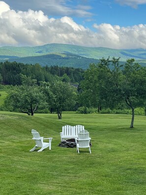 A grassy field with Adirondack chairs and a fire pit.