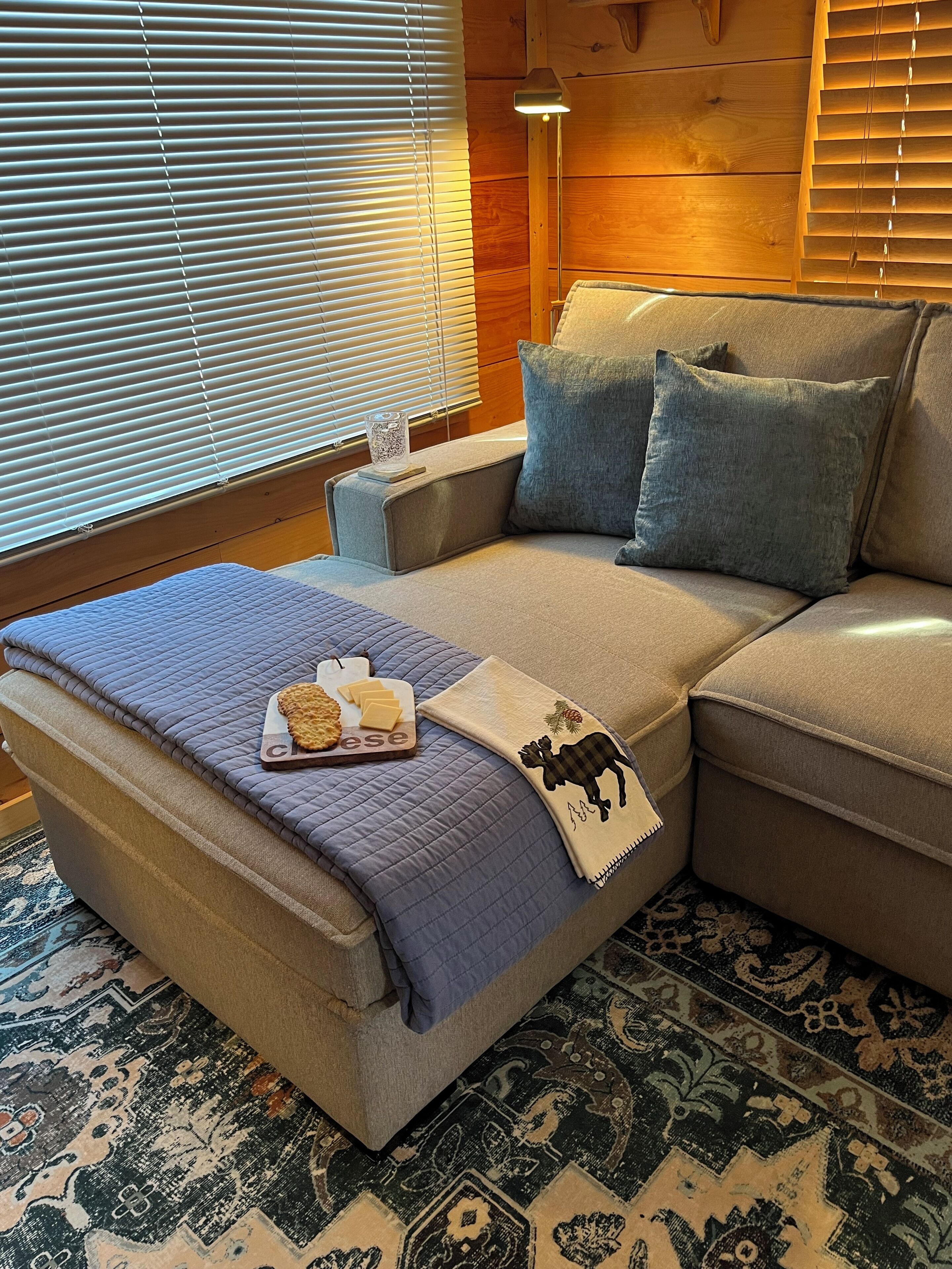 Une pièce confortable avec un canapé-lit, une couverture, un plateau de collations et un coussin décoratif.