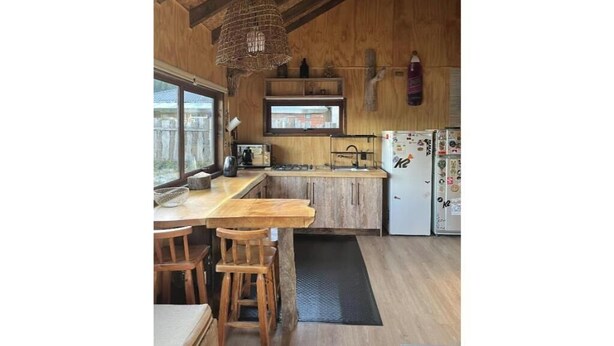 Une cuisine rustique avec des poutres en bois, un luminaire suspendu, une fenêtre et un réfrigérateur décoré d’aimants.